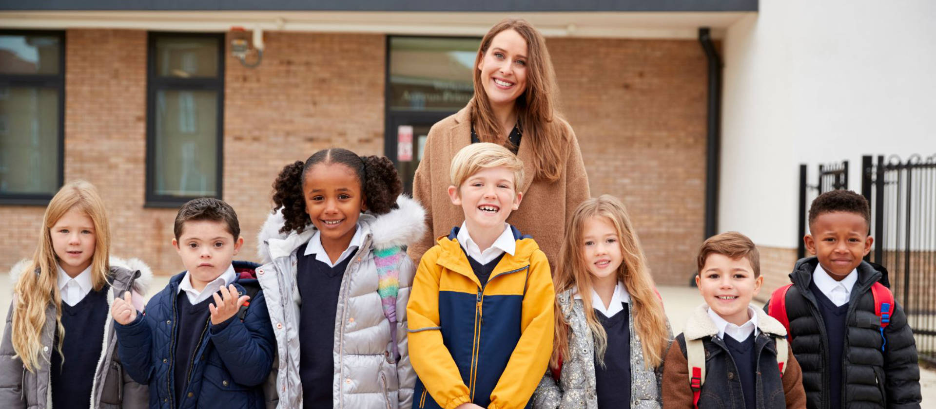 Female teacher standing with group of primary school children in the playground