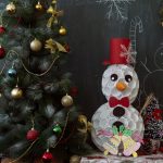 School chalboard with a decorated Christmas tree in front of it and a snowman made from white plastic cups and recycling
