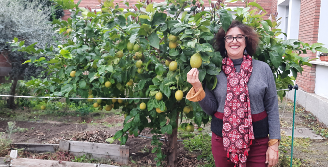 Photo of Nuria standing in front of a lemon tree holding a lemon and smiling