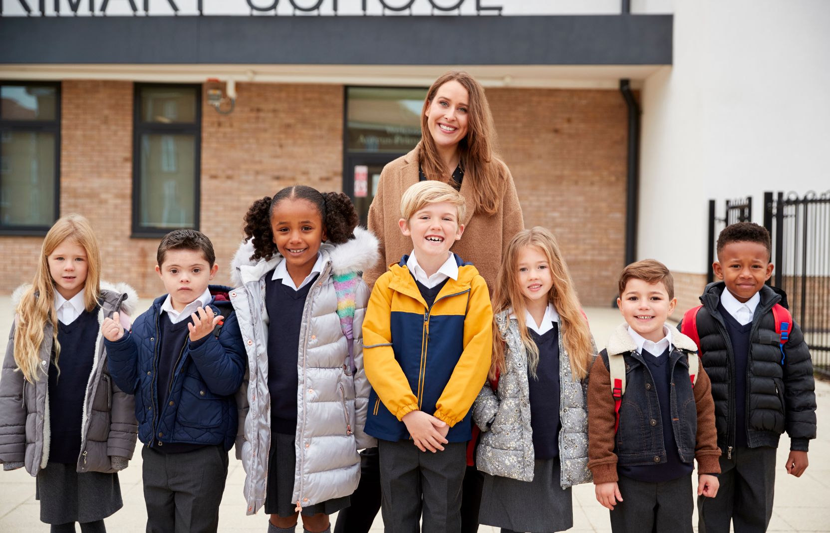 Female teacher standing with group of primary school children in the playground